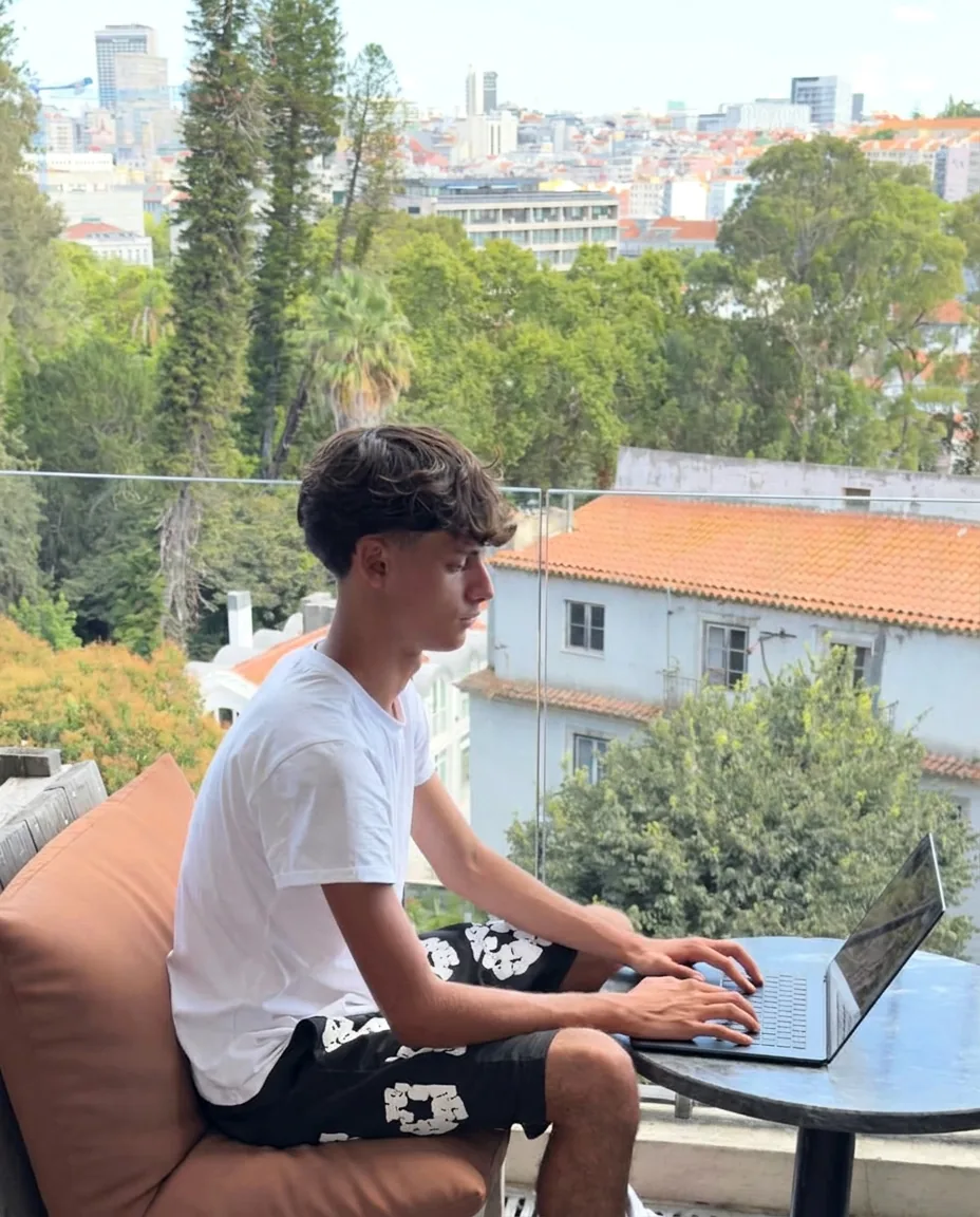 Gaspar sentado de perfil numa varanda em Lisboa, a trabalhar no portátil